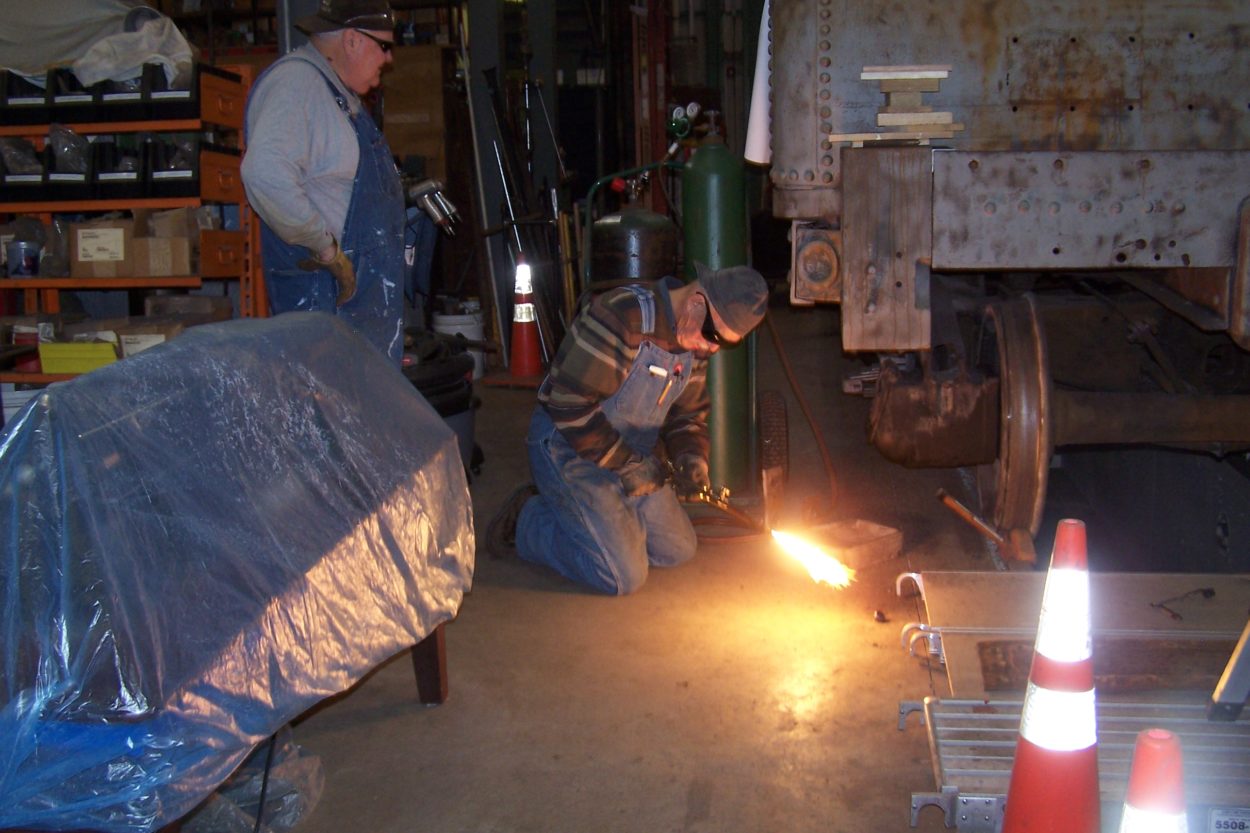 A worker lighting a torch cutter while another worker supervises