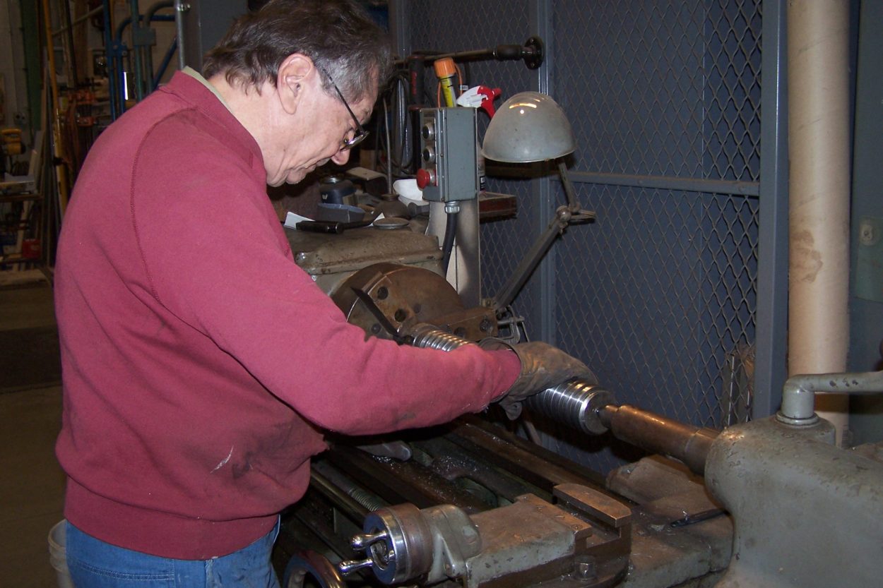 Laborer turning a piece of steel on a lathe