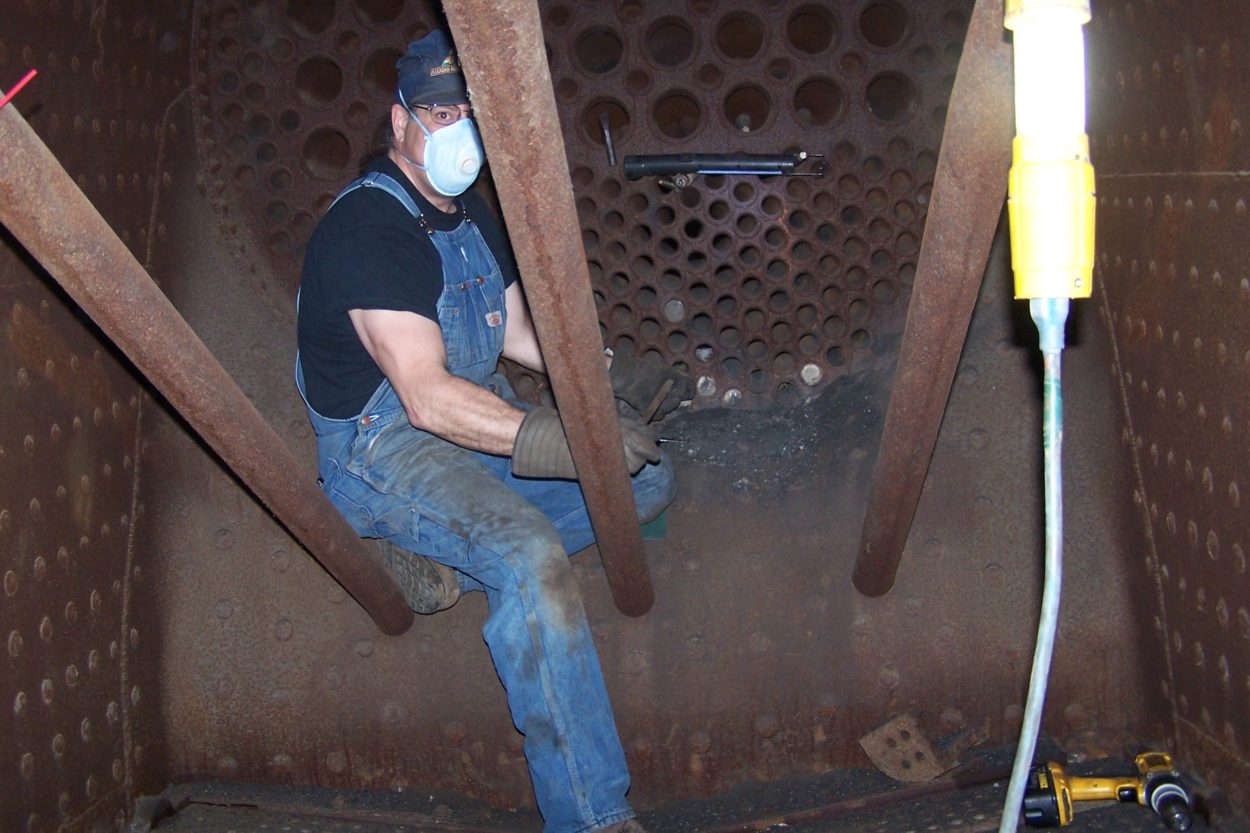 Worker inside of a steam engine's boiler restoring boiler heat pipes