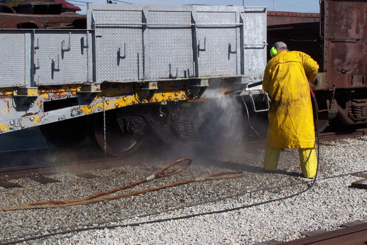 Worker dressed in yellow rain gear power washing a train car
