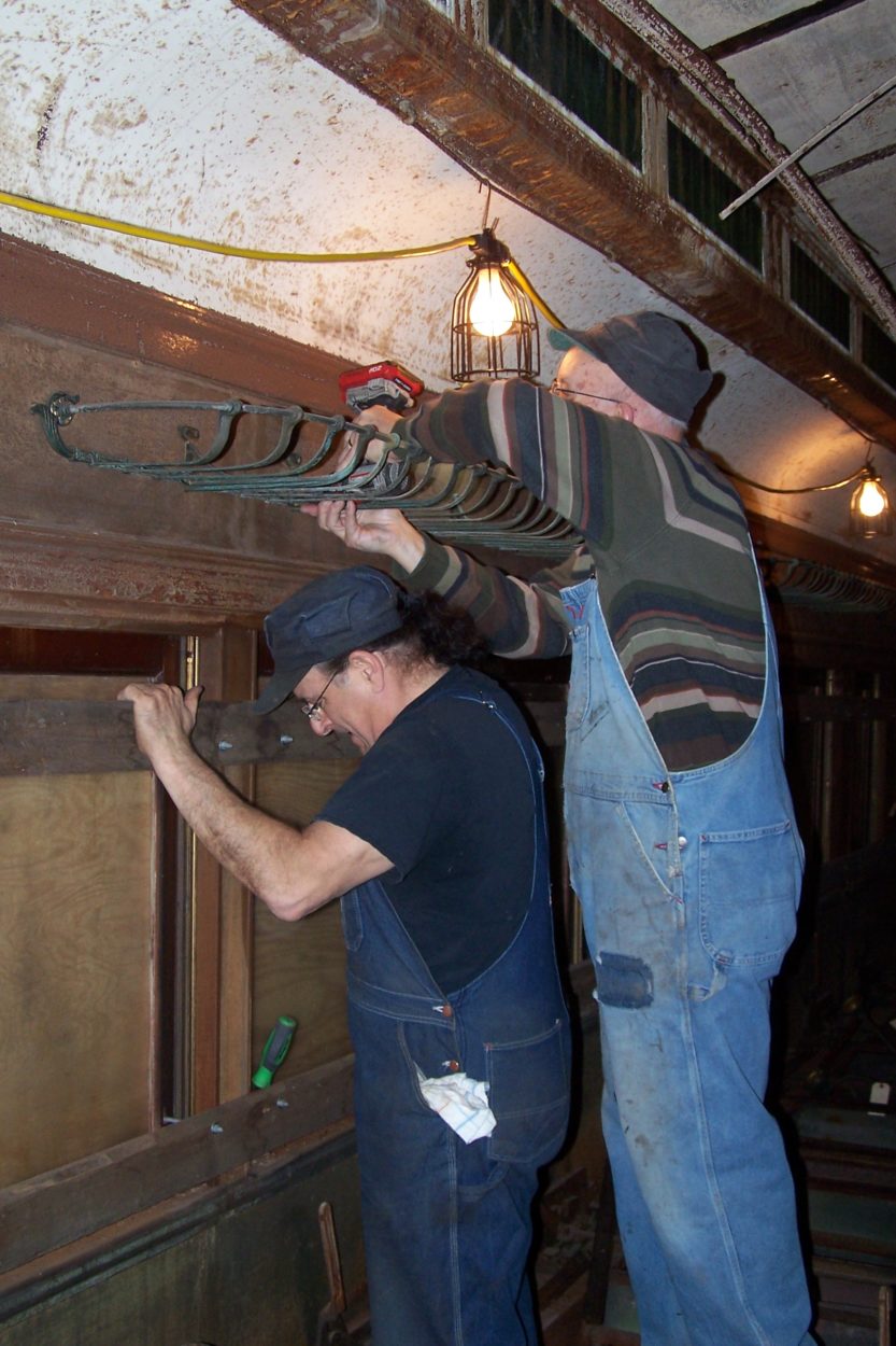 Two workers restoring a passenger car's luggage rack