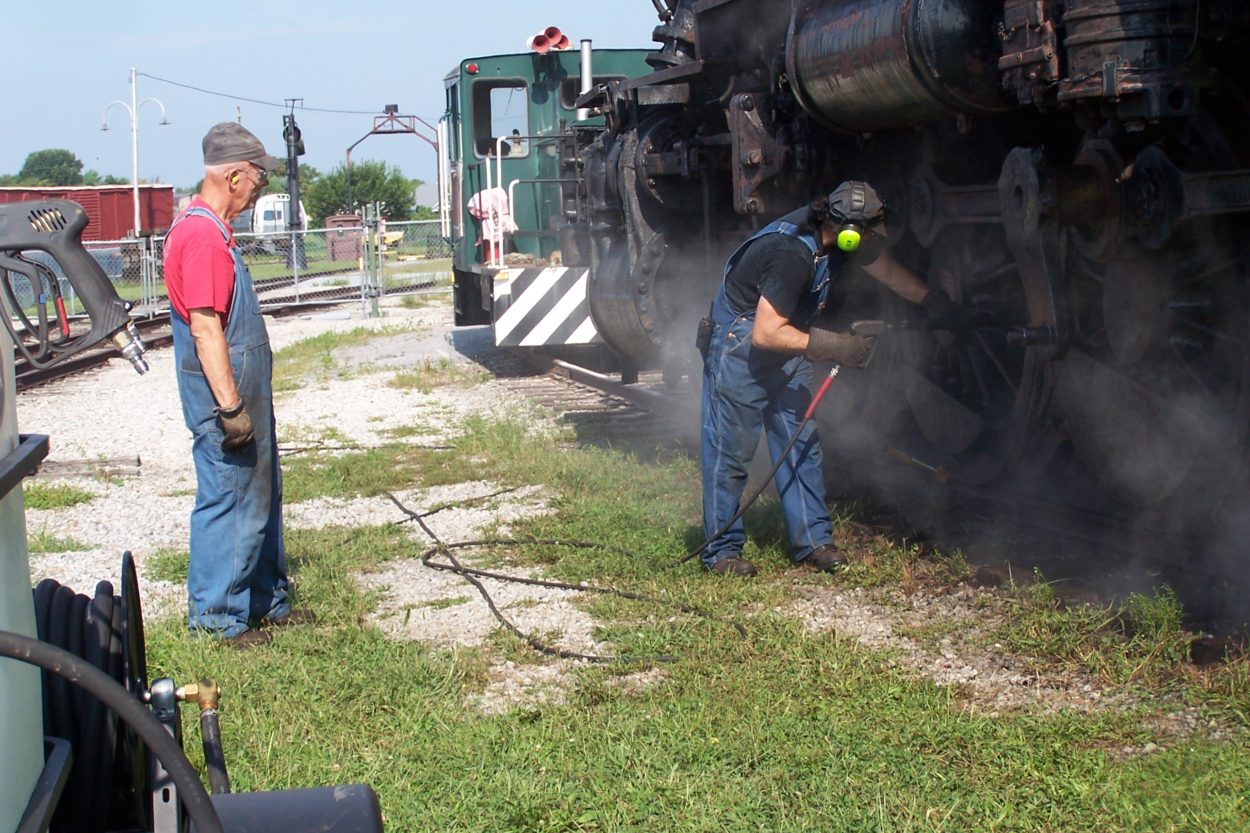 Workers pressure washing a steam locomotive's wheels