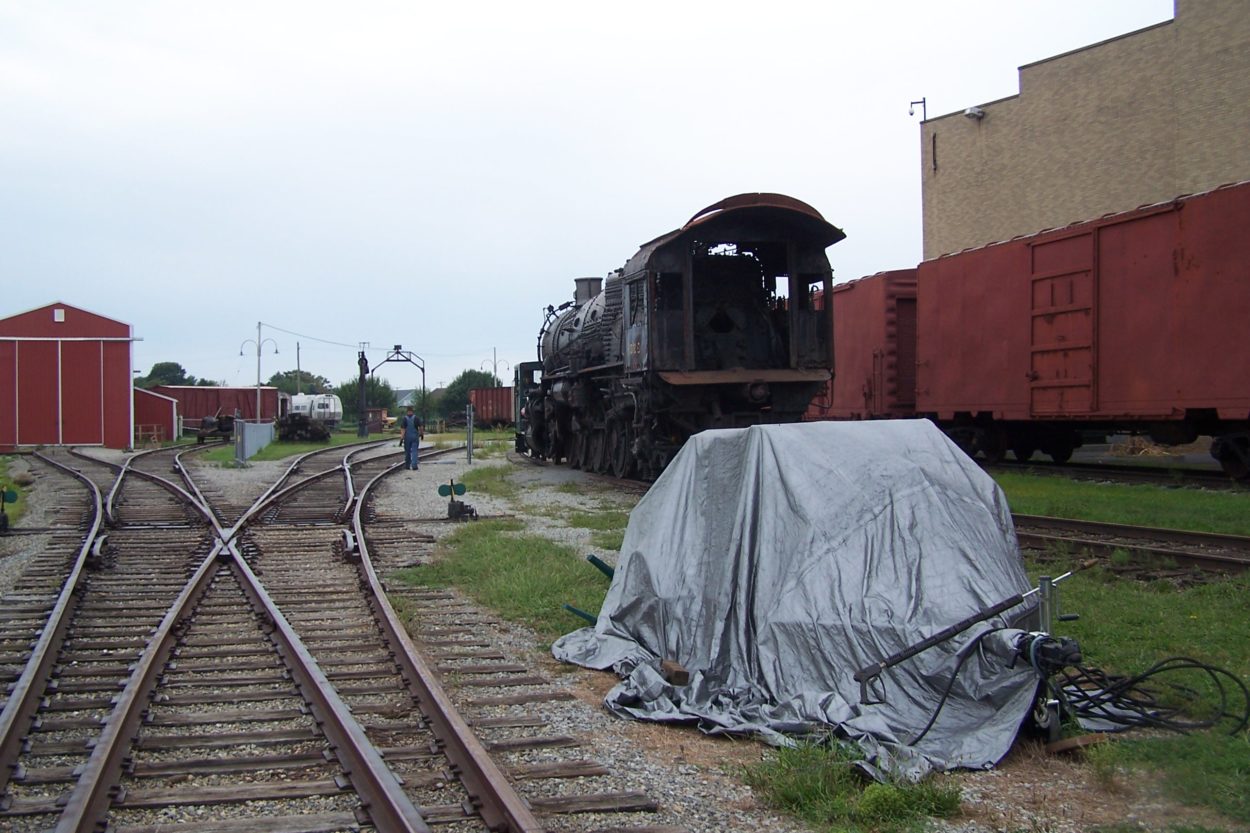 A man in the distance walking next to a locomotive parked outside of the museum