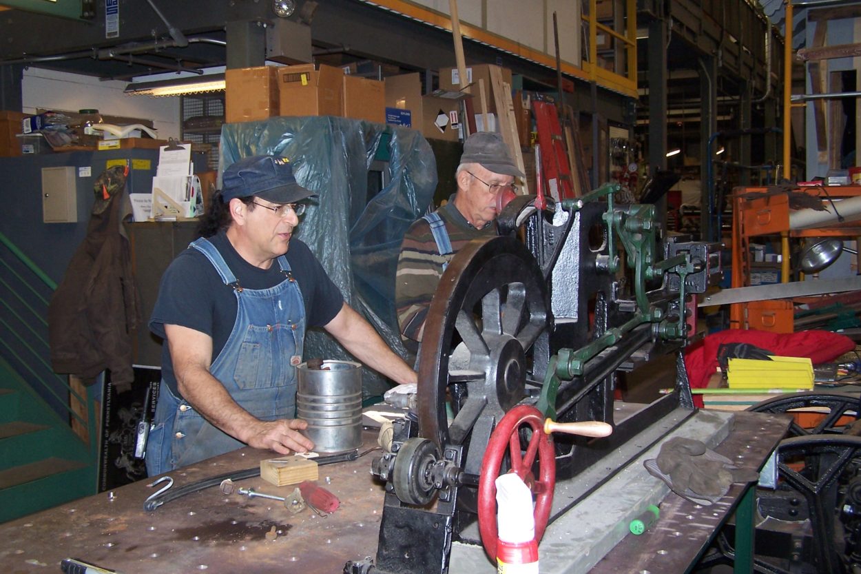 Two workers restoring a wheel system from a locomotive