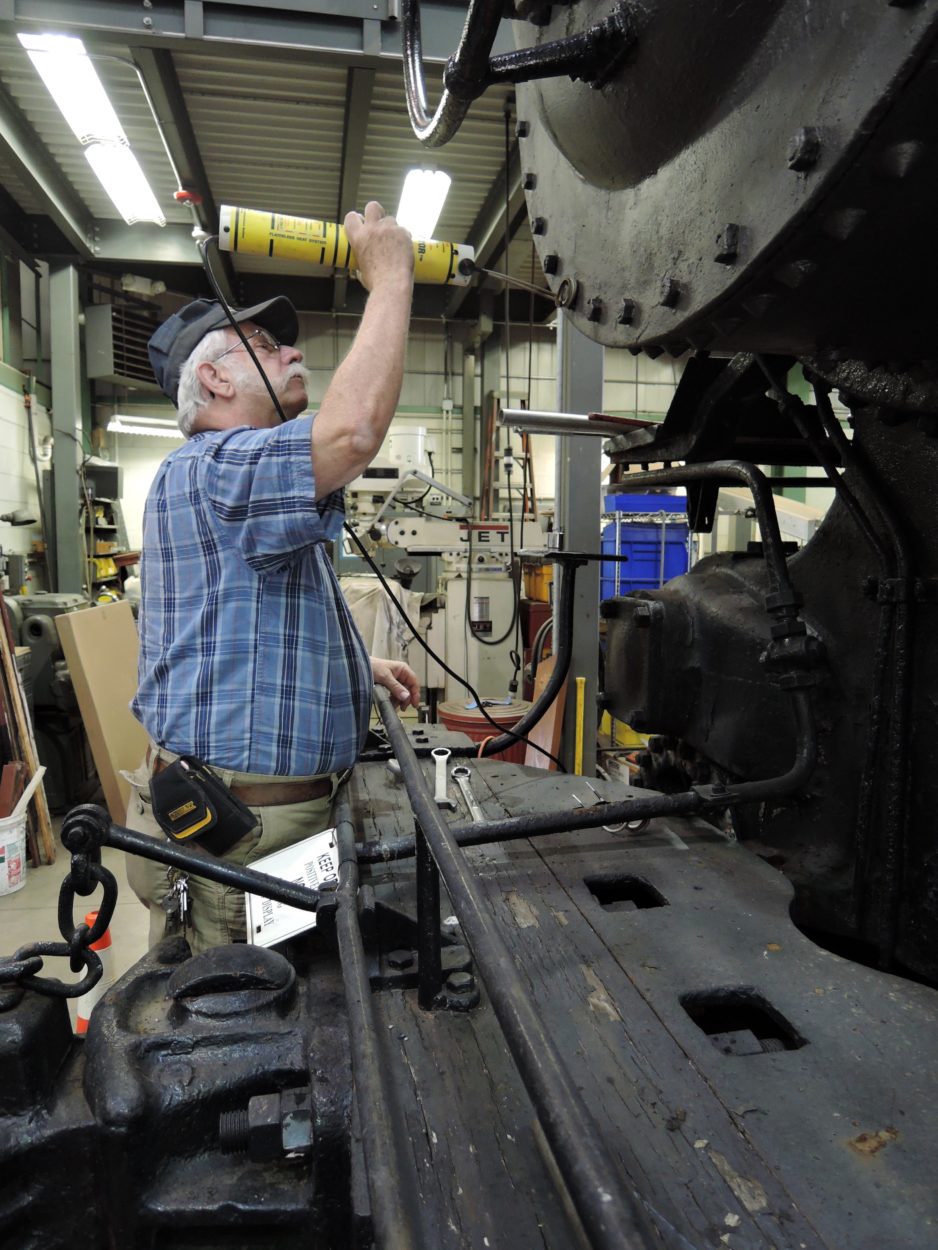 An older man sealing a bolt on the front of a black locomotive