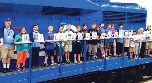 A class of children standing on the deck of a blue diesel locomotive