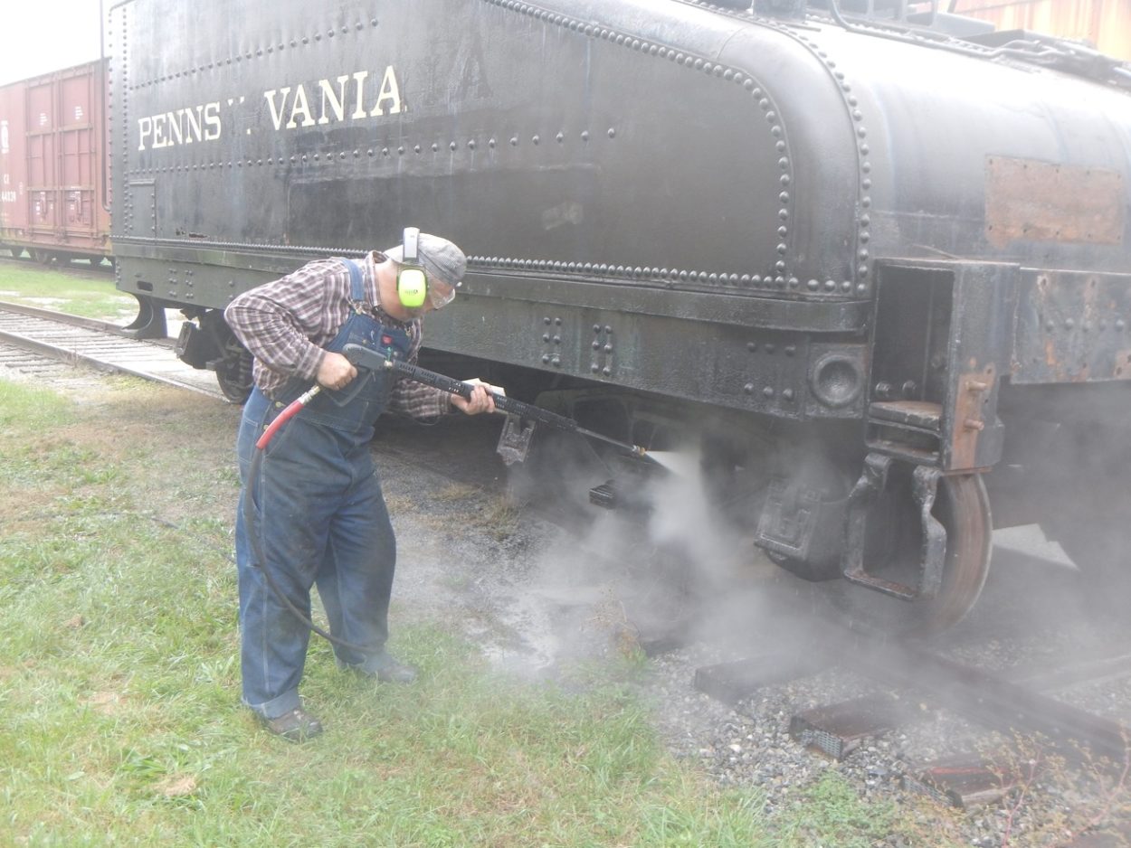 Man pressure washing the wheels of a locomotive coal car