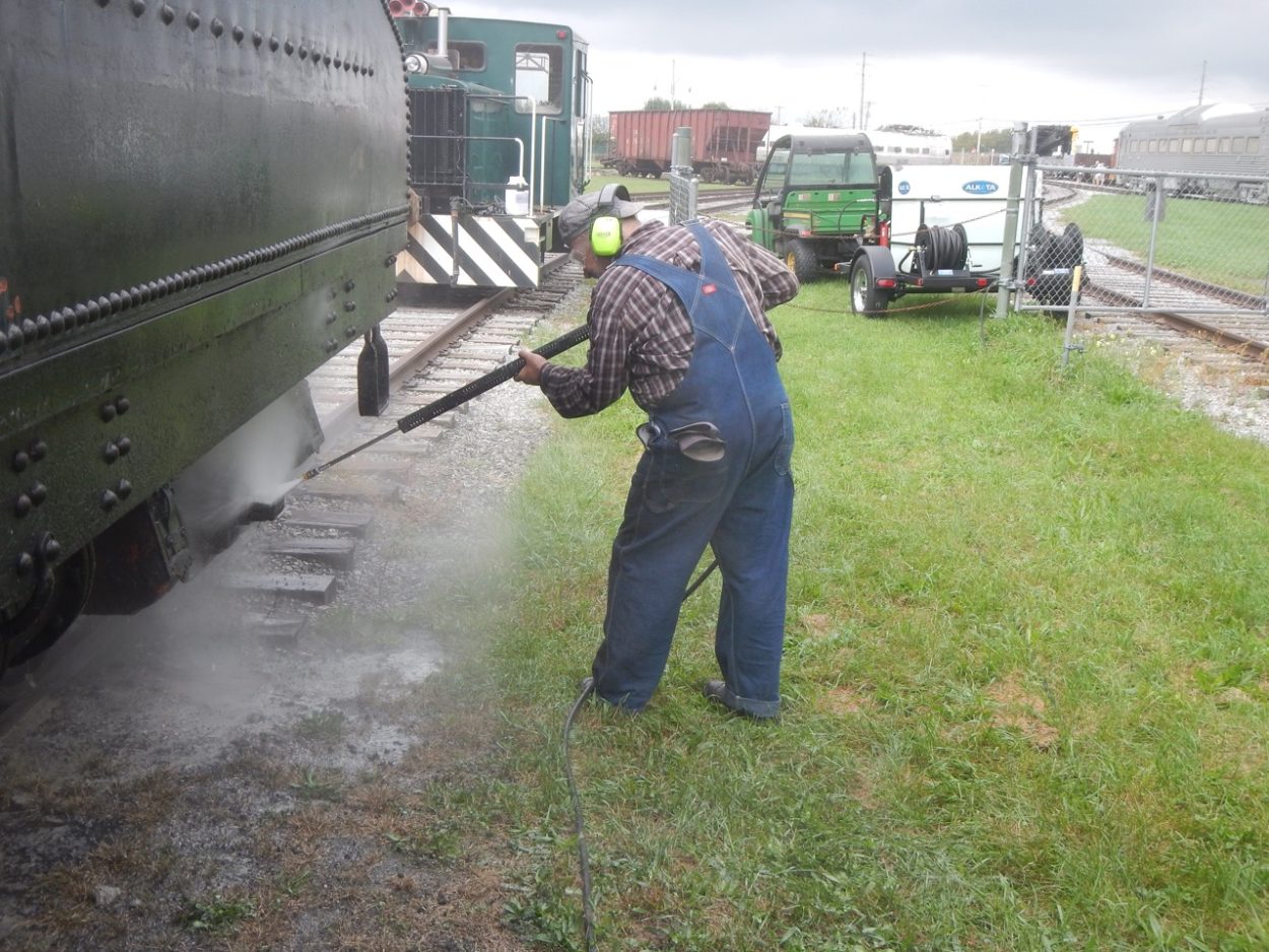 Laborer pressure washing a locomotive's coal car outdoors at the museum