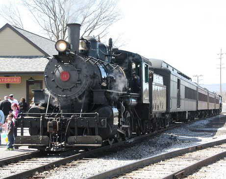 A black locomotive pulling passenger cars on a sunny winter day