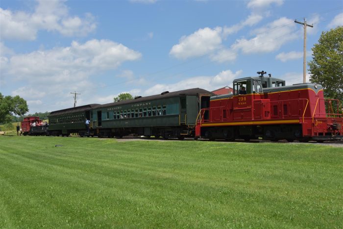 Picture of a red diesel locomotive pulling 3 passenger cars and a caboose on a sunny day