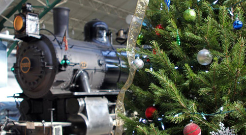 photo of a black locomotive on the left side of the picture, and a decorated Christmas tree on the right.
